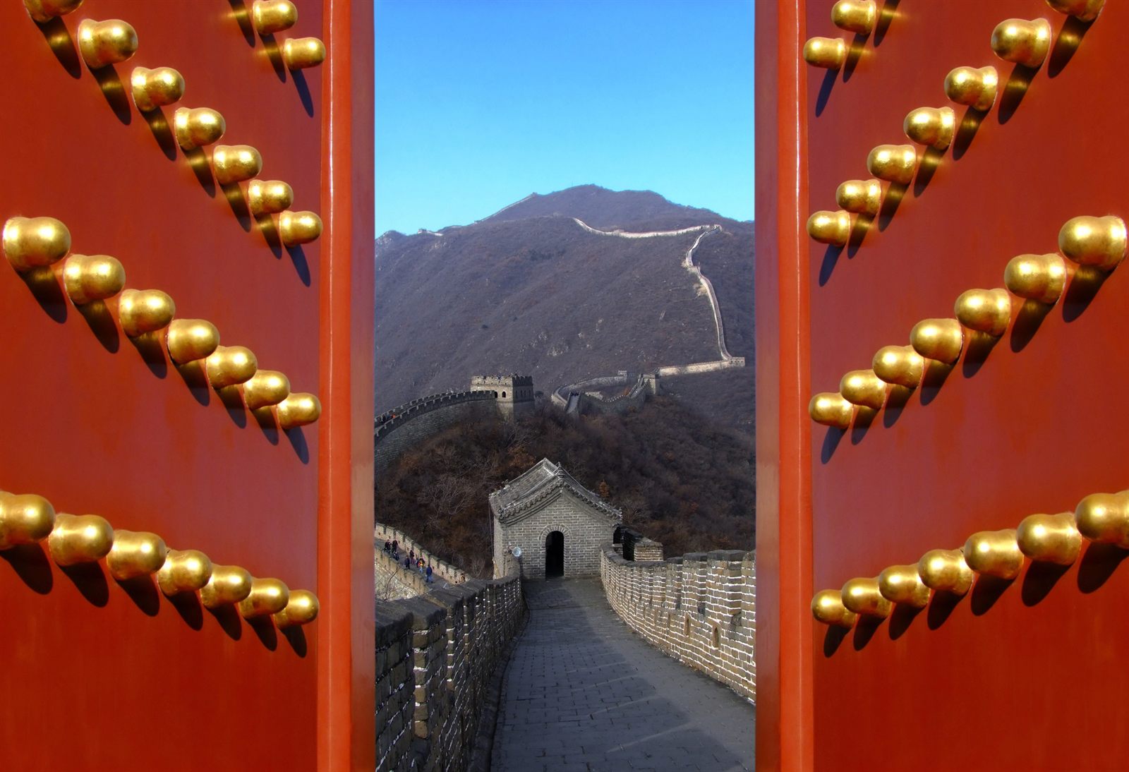 View of the Great Wall framed by red doors studded with golden knobs
